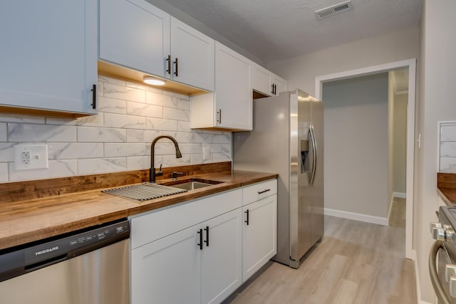 kitchen with visible vents, appliances with stainless steel finishes, white cabinetry, a sink, and wood counters