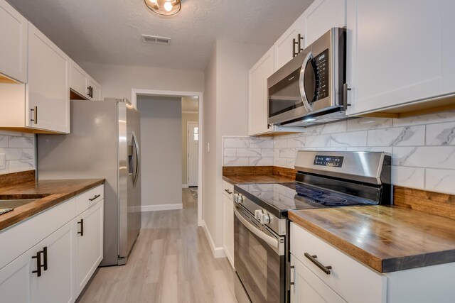 kitchen with butcher block countertops, light wood-style floors, appliances with stainless steel finishes, and white cabinetry