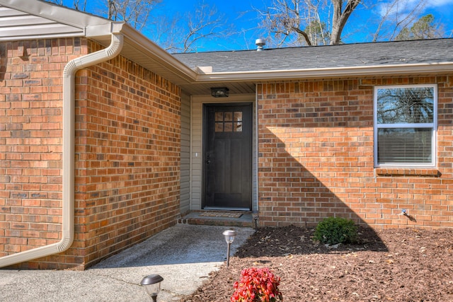 entrance to property with brick siding and roof with shingles