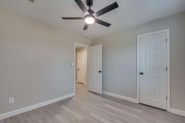 unfurnished bedroom featuring a ceiling fan, light wood-style flooring, baseboards, and a textured ceiling