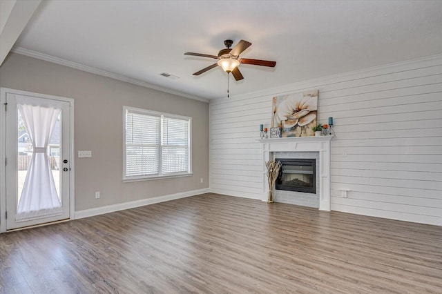 unfurnished living room featuring crown molding, ceiling fan, wood walls, and hardwood / wood-style floors