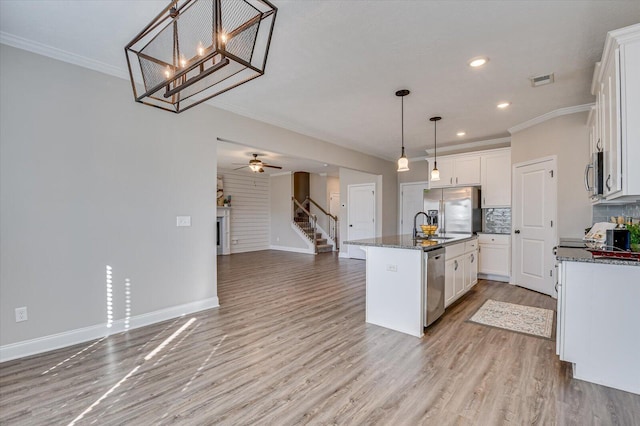 kitchen with decorative light fixtures, white cabinets, stainless steel appliances, and a center island with sink