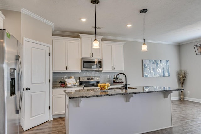 kitchen featuring white cabinets, appliances with stainless steel finishes, pendant lighting, and a center island with sink