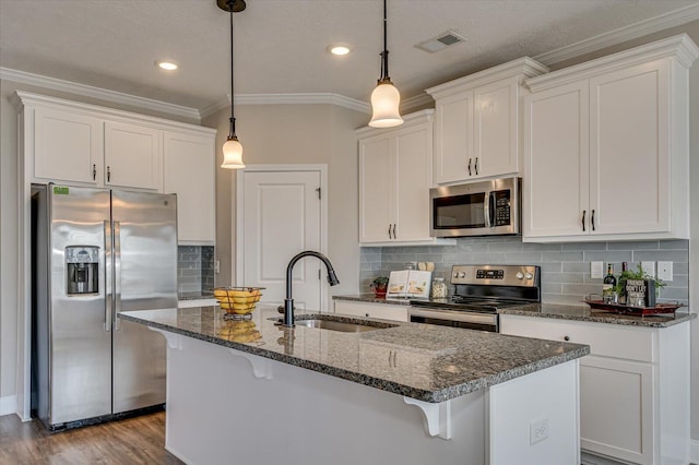 kitchen featuring appliances with stainless steel finishes, decorative light fixtures, dark stone counters, sink, and a kitchen island with sink