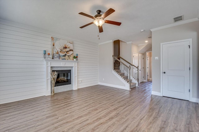 unfurnished living room featuring wood walls, ceiling fan, ornamental molding, and light hardwood / wood-style flooring