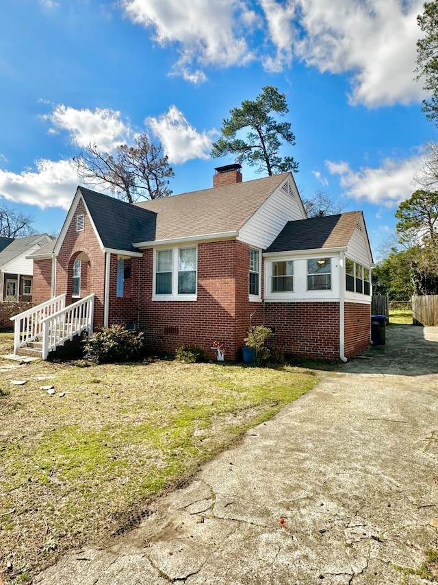 view of front of property with brick siding, roof with shingles, crawl space, a chimney, and a front yard