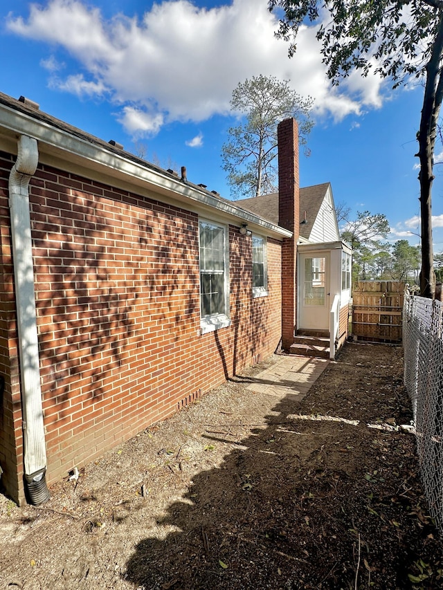 rear view of property featuring entry steps, brick siding, a chimney, and fence private yard