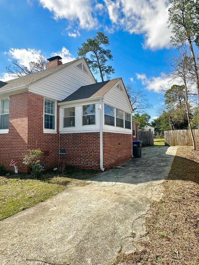 view of property exterior featuring brick siding, a chimney, and fence