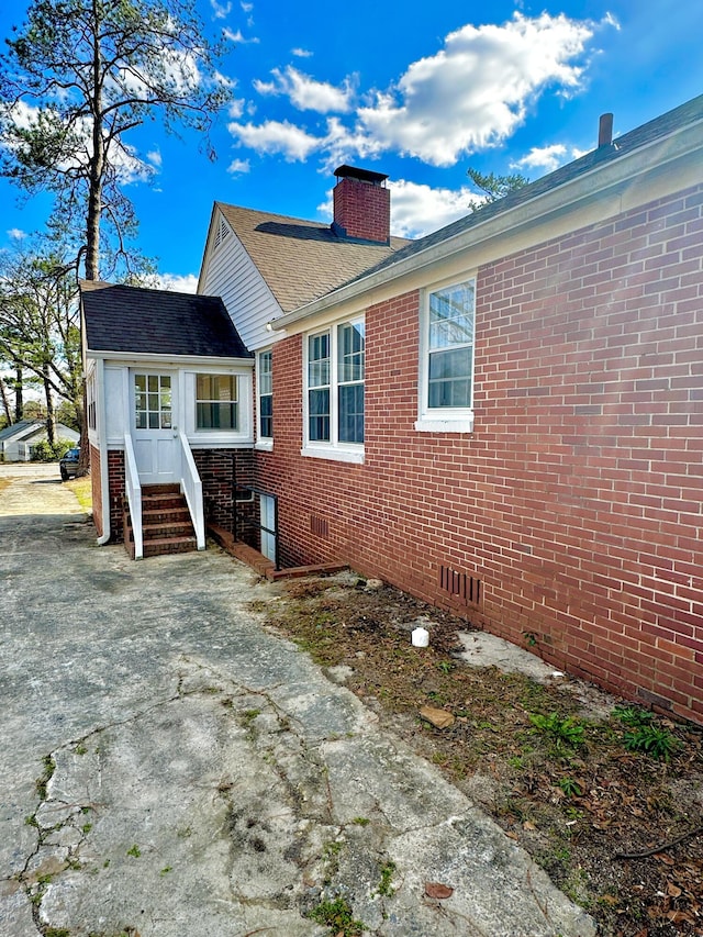 view of home's exterior with roof with shingles, brick siding, crawl space, and a chimney