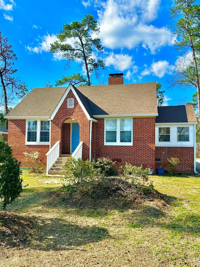 ranch-style house with entry steps, brick siding, a chimney, and a front lawn