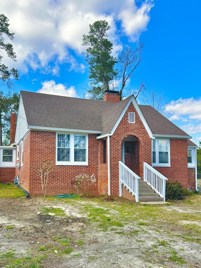 view of front of property featuring brick siding, a chimney, and a shingled roof