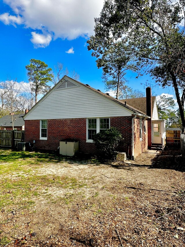 view of home's exterior with a chimney, fence, a lawn, and brick siding