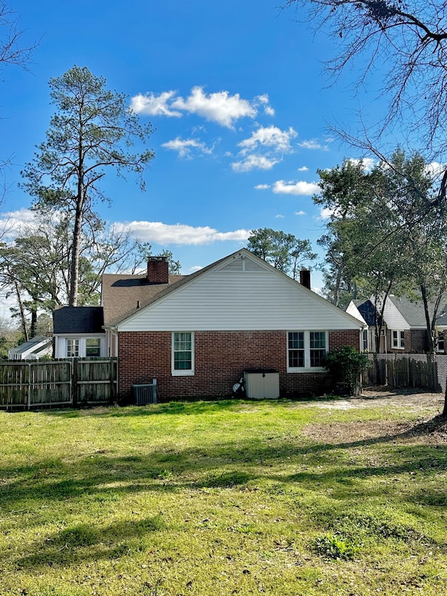 view of property exterior with brick siding, a yard, a chimney, and fence