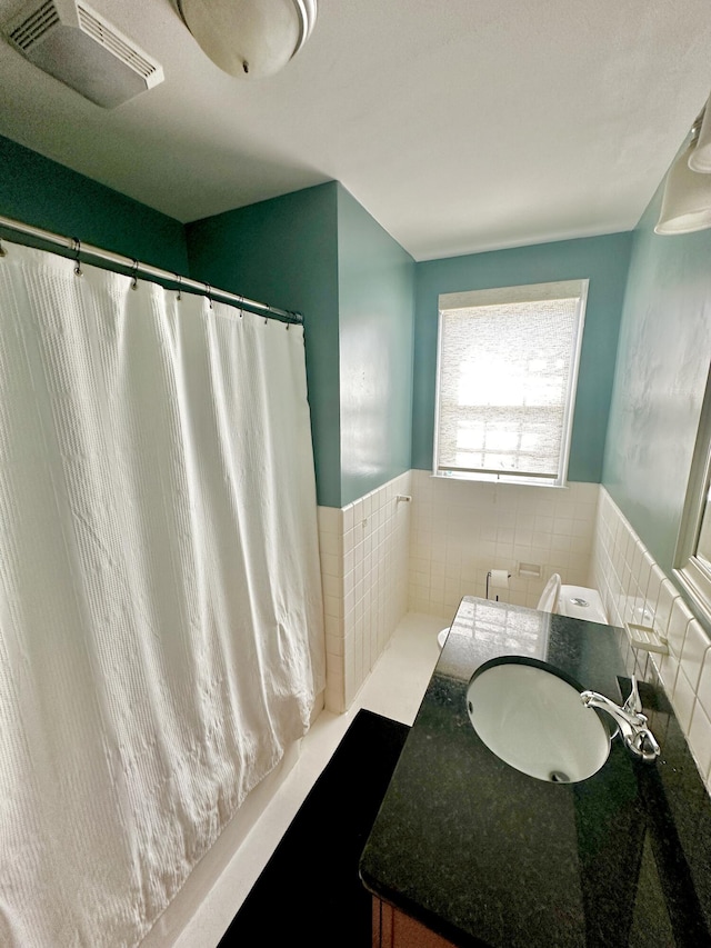 bathroom with a wainscoted wall, vanity, visible vents, and tile walls