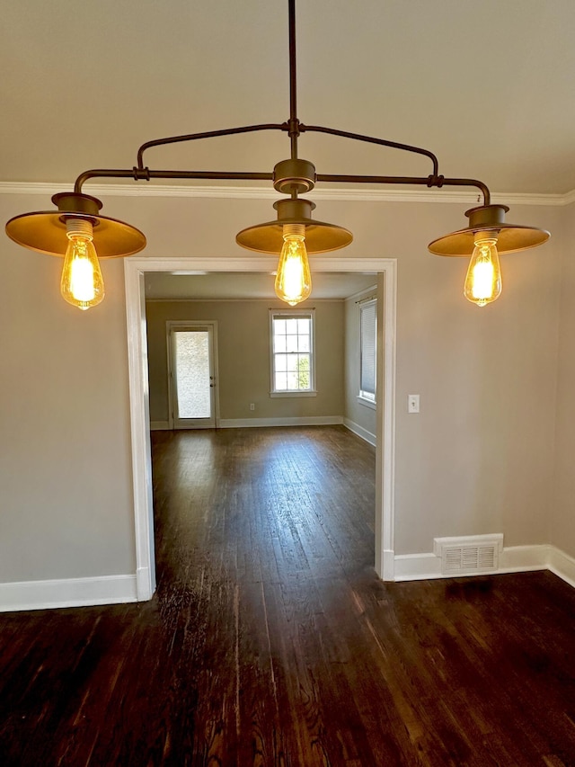 empty room with baseboards, visible vents, dark wood-type flooring, and ornamental molding