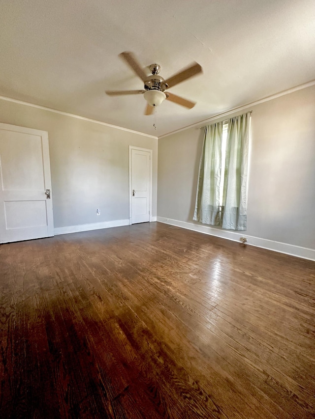 empty room featuring dark wood-type flooring, ornamental molding, and baseboards