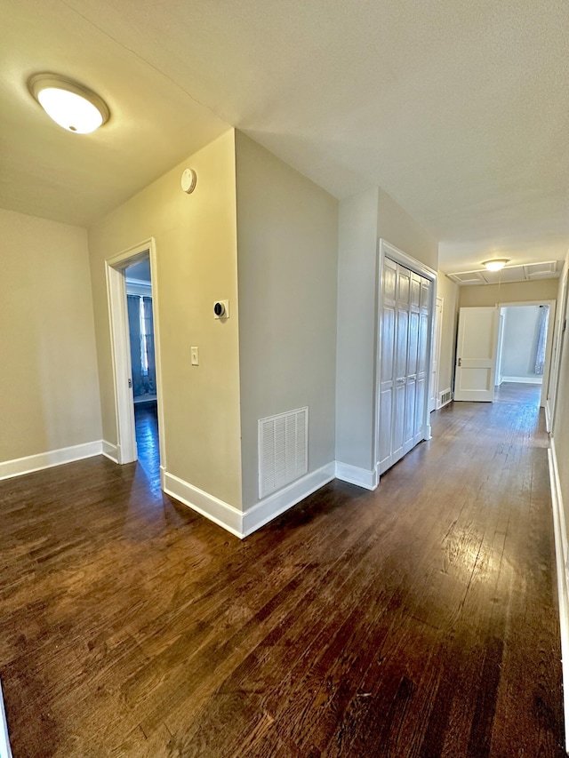 interior space with dark wood-type flooring, attic access, visible vents, and baseboards