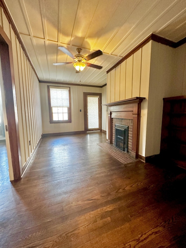 unfurnished living room featuring crown molding, a fireplace, a ceiling fan, and dark wood-type flooring