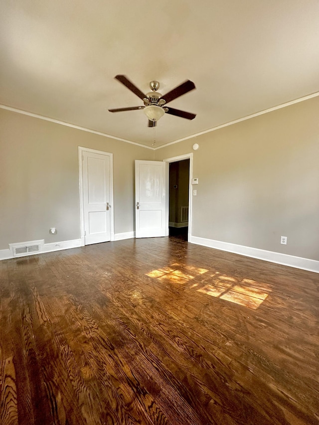 spare room with dark wood-style floors, visible vents, crown molding, and baseboards