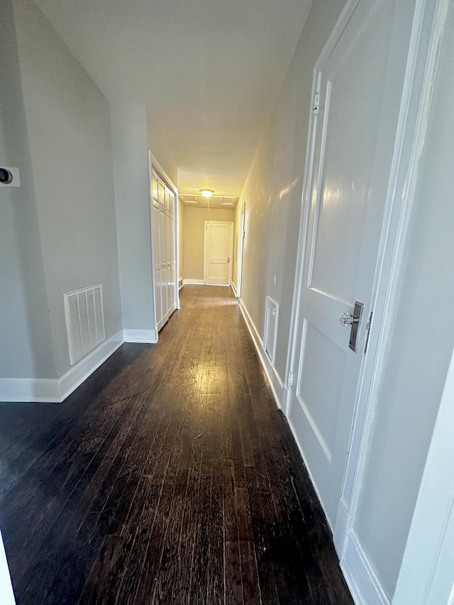 hall featuring baseboards, attic access, visible vents, and dark wood-type flooring