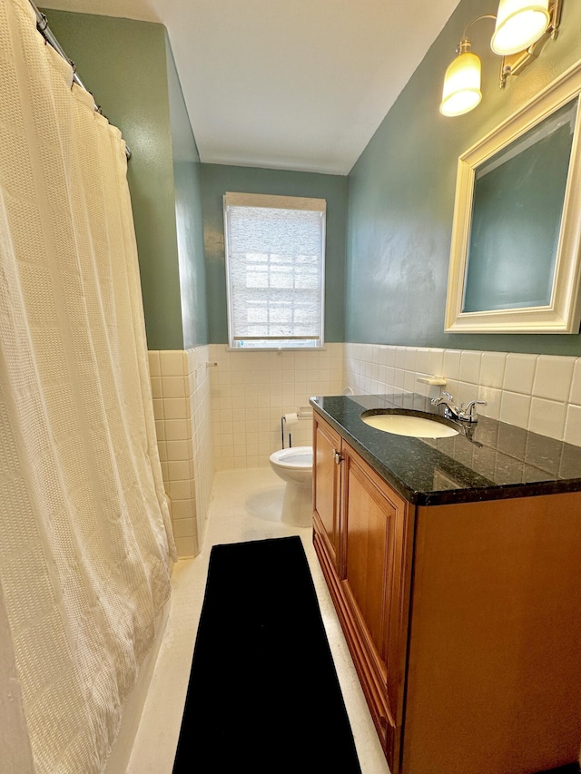 full bathroom with toilet, wainscoting, vanity, and tile walls