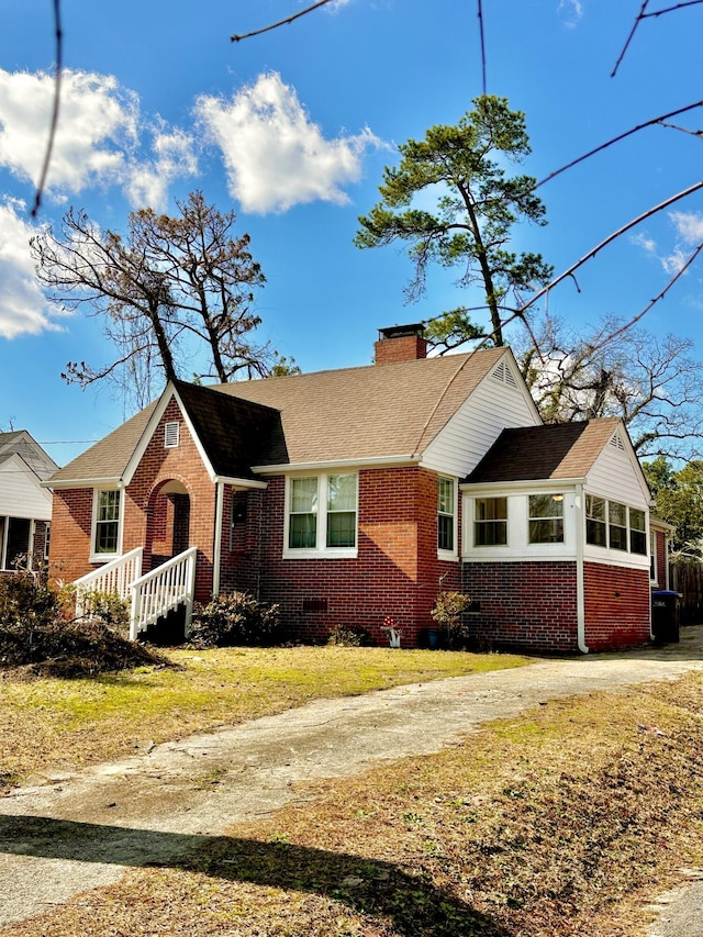 ranch-style home featuring driveway, brick siding, a chimney, and a front yard