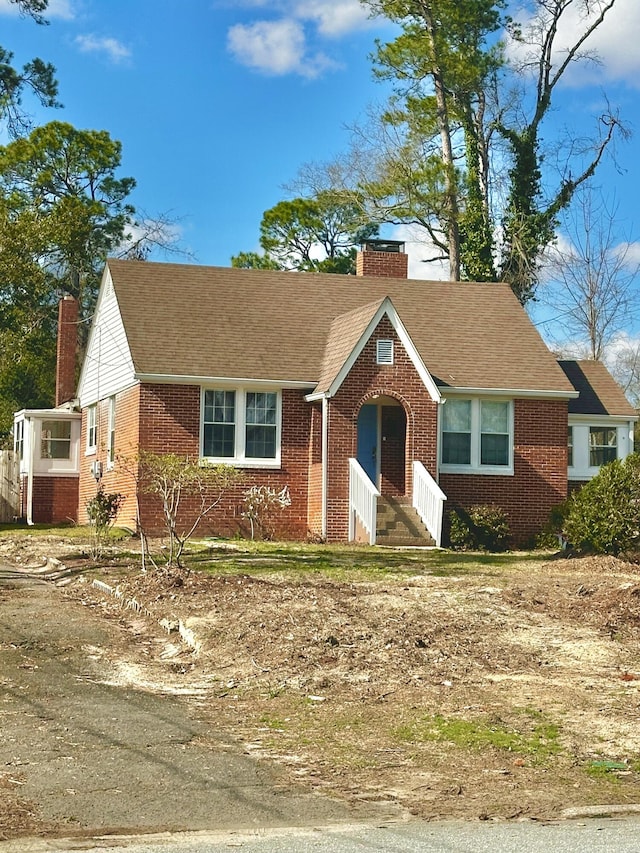 view of front of house with entry steps, a shingled roof, a chimney, and brick siding