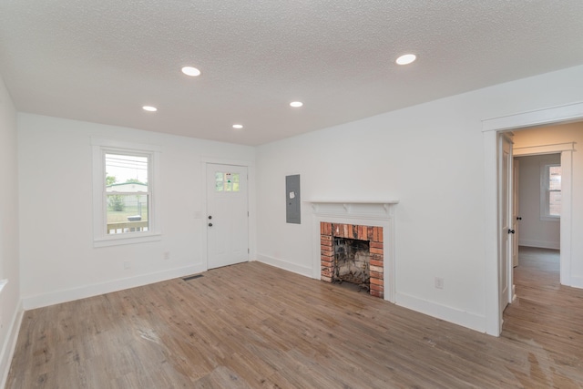 unfurnished living room with a fireplace, a textured ceiling, hardwood / wood-style flooring, and electric panel