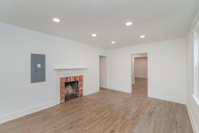 unfurnished living room with light wood-type flooring, a textured ceiling, electric panel, and a brick fireplace