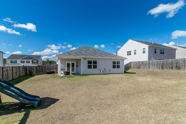 rear view of house featuring a playground, a shingled roof, a yard, and a fenced backyard