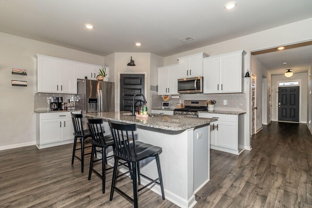 kitchen with a breakfast bar area, dark wood-style flooring, tasteful backsplash, a sink, and stainless steel appliances