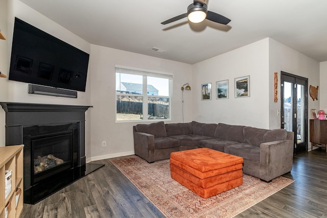 living area featuring a glass covered fireplace, a ceiling fan, wood finished floors, and visible vents