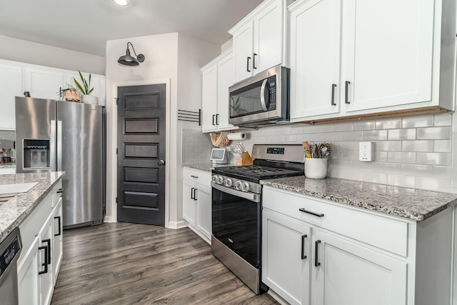 kitchen featuring white cabinets, light stone countertops, stainless steel appliances, decorative backsplash, and dark wood-style floors