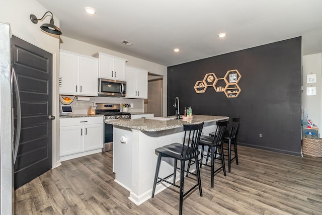 kitchen featuring appliances with stainless steel finishes, an accent wall, wood finished floors, and white cabinetry