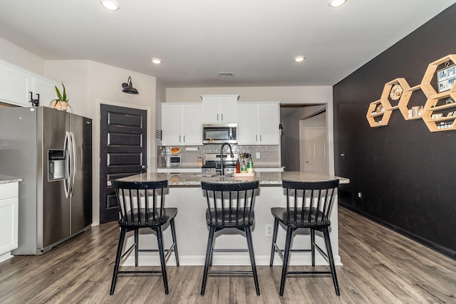 kitchen featuring wood finished floors, a breakfast bar area, white cabinets, appliances with stainless steel finishes, and backsplash