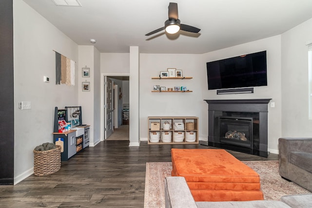 living area with dark wood-style flooring, a ceiling fan, a fireplace with flush hearth, and baseboards
