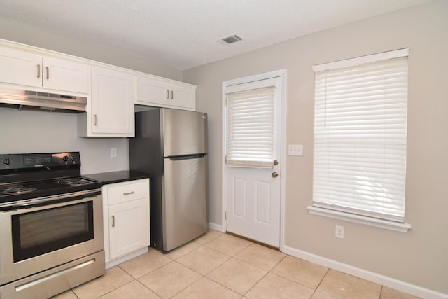 kitchen with light tile patterned floors, stainless steel appliances, dark countertops, white cabinetry, and under cabinet range hood