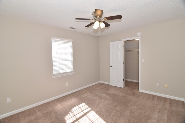 unfurnished bedroom with a textured ceiling, a spacious closet, carpet floors, and visible vents