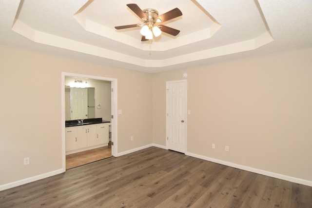 unfurnished bedroom with baseboards, connected bathroom, wood finished floors, a tray ceiling, and a sink