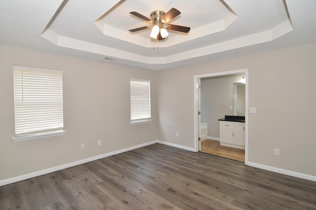 unfurnished bedroom with a tray ceiling, dark wood finished floors, visible vents, and baseboards