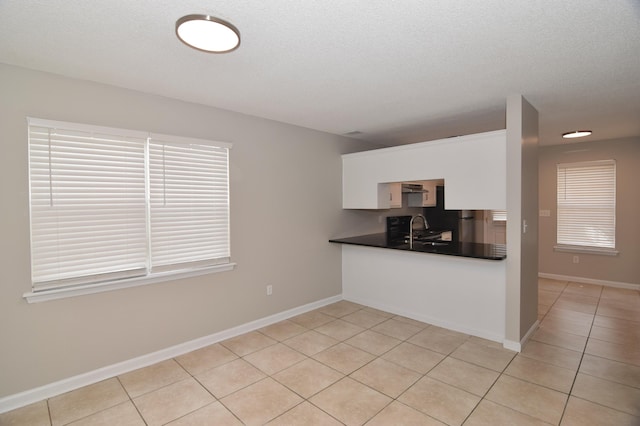 kitchen with dark countertops, a sink, light tile patterned flooring, and baseboards