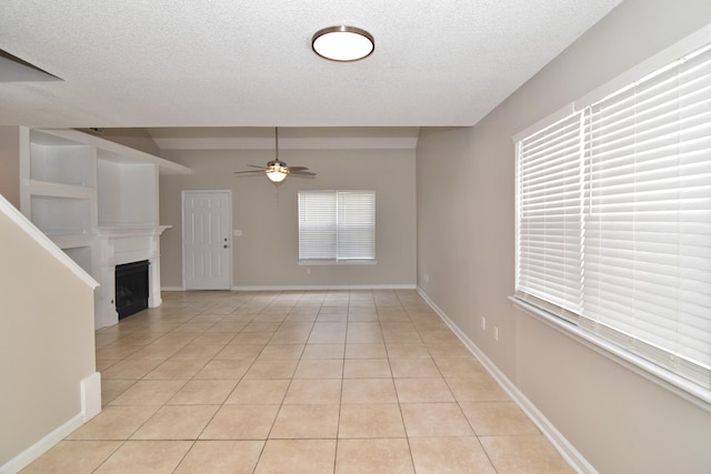 interior space featuring a fireplace, light tile patterned floors, a ceiling fan, a textured ceiling, and baseboards