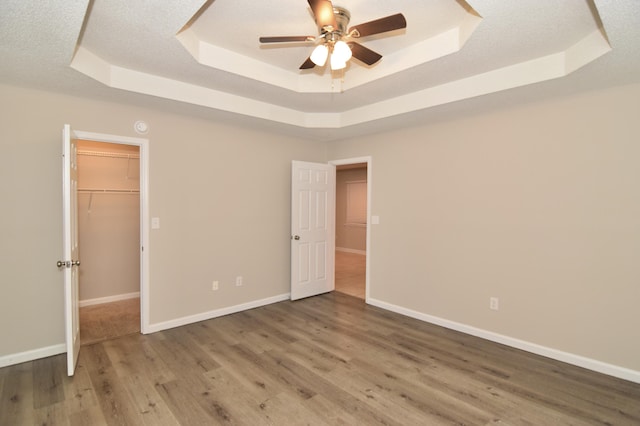 unfurnished bedroom with a textured ceiling, a tray ceiling, wood finished floors, and baseboards