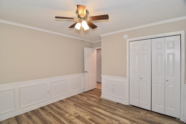 unfurnished bedroom with a wainscoted wall, crown molding, a closet, a ceiling fan, and wood finished floors