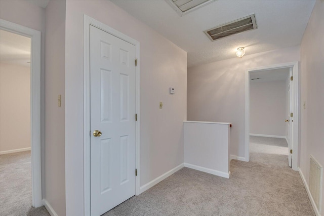 hall featuring visible vents, an upstairs landing, baseboards, and carpet flooring