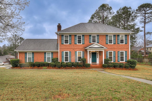 view of front of house featuring fence, a shingled roof, a chimney, a front lawn, and brick siding