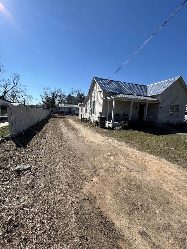 view of property exterior featuring covered porch, metal roof, dirt driveway, and fence