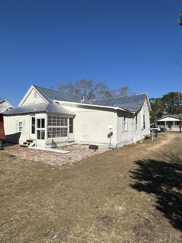 rear view of property featuring entry steps, metal roof, and a lawn