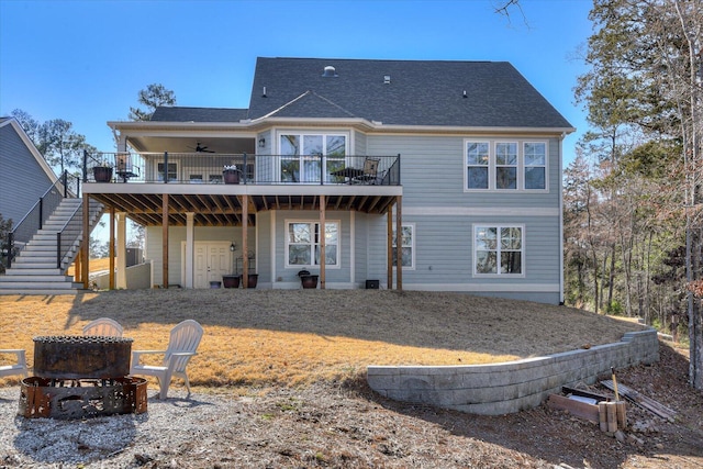 back of property with a deck, an outdoor fire pit, a ceiling fan, roof with shingles, and stairway