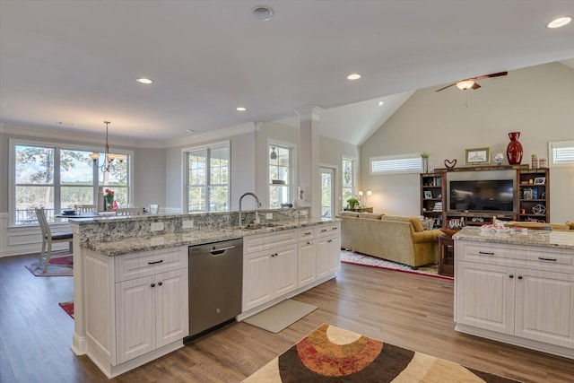 kitchen featuring open floor plan, hanging light fixtures, stainless steel dishwasher, white cabinetry, and a sink